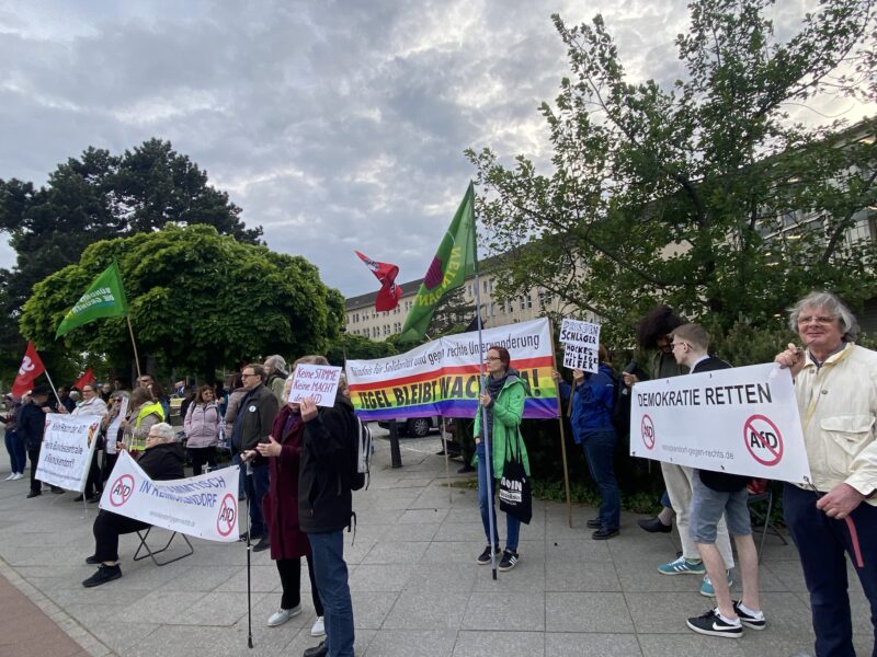 Foto von einer Kundgebung vor dem Maestral am 07.05.2024 anlässlich des AfD stammtisches. Auf dem Foto sieht man viele Personen die Fahnen und Banner halten. Darauf steht u.a. "Demokratie retten", "Nazis nein Danke", "Tegel bleibt wachsam". 